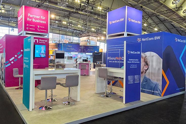 Großzügiger Messestand von NetCom BW und Plusnet mit markanten Deckenelementen, Beratungsplätzen und aufmerksamkeitsstarker Markenpräsentation.